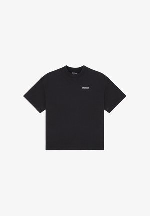 Musta lyhythihainen t-paita, jossa "WRSTBHVR" on painettu pienin valkoisin kirjaimin vasempaan rintaan ja kauluksen sisäpuolelle.