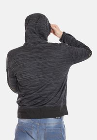 Haut à capuche noir, texturé, avec une capuche ajustée, un cordon de serrage réglable et des bords noirs au bas et aux poignets, porté à l'envers.