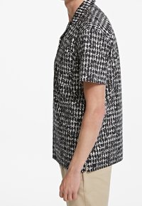 Camicia a maniche corte in tessuto bianco e nero con un motivo geometrico, caratterizzata da una vestibilità rilassata e un collo standard.