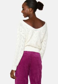 Witte, opengehaakte trui met V-hals en chevronpatroon; gedragen met hoog-waist, pruimen corduroy broek.
