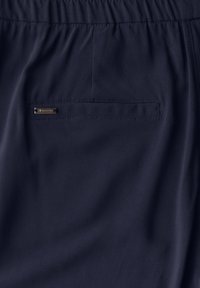 Navy blue fabric shorts with a smooth texture, elastic waistband, and a small metallic brand tag on the back pocket.