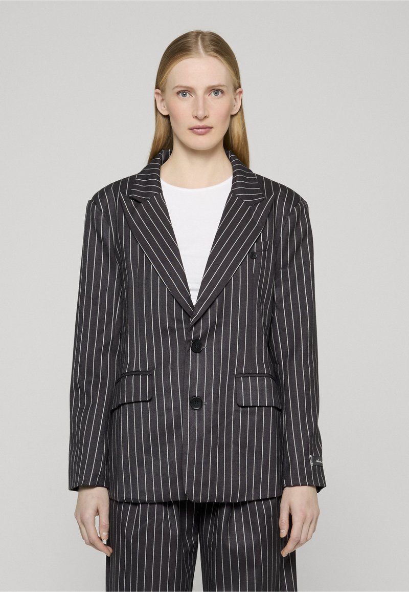 Svart blazer med nålestriper, strukturert silhuett, brede slag, to knapper og to fremre lommer. Stoffet har en glatt tekstur.