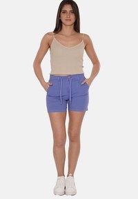 Pantaloni corti leggeri in lavanda con vita a cordoncino e tasche frontali, abbinati a una canotta beige a costine. Sneakers bianche completano l'outfit.