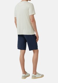 Maglietta grigia chiara a maniche corte, pantaloni corti blu scuro e scarpe da ginnastica bianche. Design semplice e casual con vestibilità comoda e texture morbida.