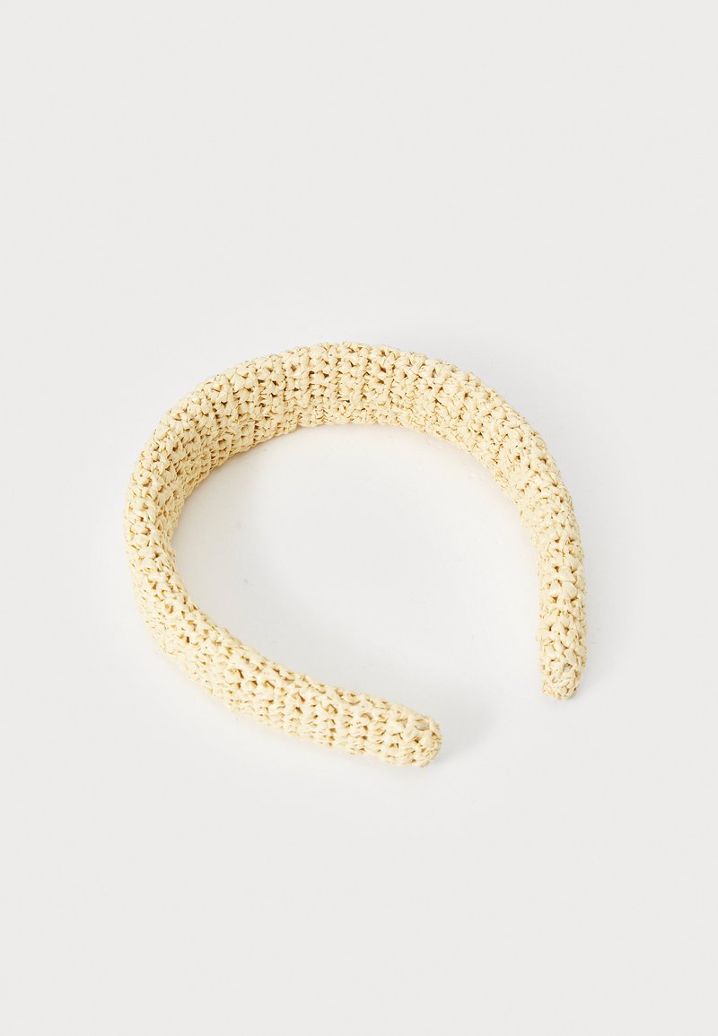 Bežs austs matu lente, izgatavota no teksturēta materiāla, ar apļa formu un gludām malām, piemērota matu fiksēšanai.