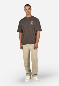 Hnedé bavlnené tričko s krátkym rukávom, zdobené svetlou potlačou na hrudi. Nosí sa s béžovými nohavicami a bielymi teniskami.