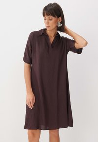 Kurzärmliges, locker sitzendes Kleid in dunklem Burgunderrot, mit aufgesetztem Kragen und weichem, strukturiertem Stoff. Keine Muster oder sichtbare Hardware.