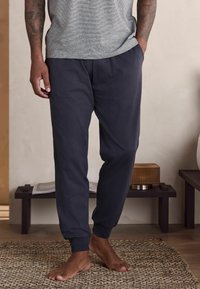 Mørkeblå joggerbukser lavet af blødt stof, med elastiske manchetter og lommer, båret med en gråstribet t-shirt.