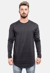 Langärmliges, dunkelgraues Shirt mit Rundhalsausschnitt, aus einem weichen Material gefertigt, mit abgerundetem Saum und enganliegenden Ärmeln. Wird mit hellen Jeans aus Denim kombiniert.