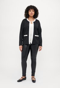 Musthave tekstuuriga must kardigan valgete äärte ja taskutega, kantud valge t-särgi peal ning sobitatud mustade legginsite ja tasaste kingadega.