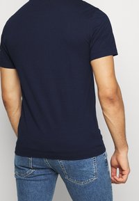 Mörkblå bomull t-shirt med korta ärmar, figurnära design och rundad halsringning. Lätt texturerat tyg, enfärgad utan mönster eller dekorationer.