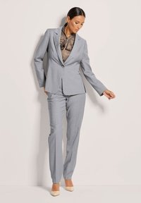 Helles graues maßgeschneidertes Anzug mit einem taillierten Blazer und geraden Hosenbeinen, kombiniert mit einer taupefarbigen Satinbluse und beigen Heels.