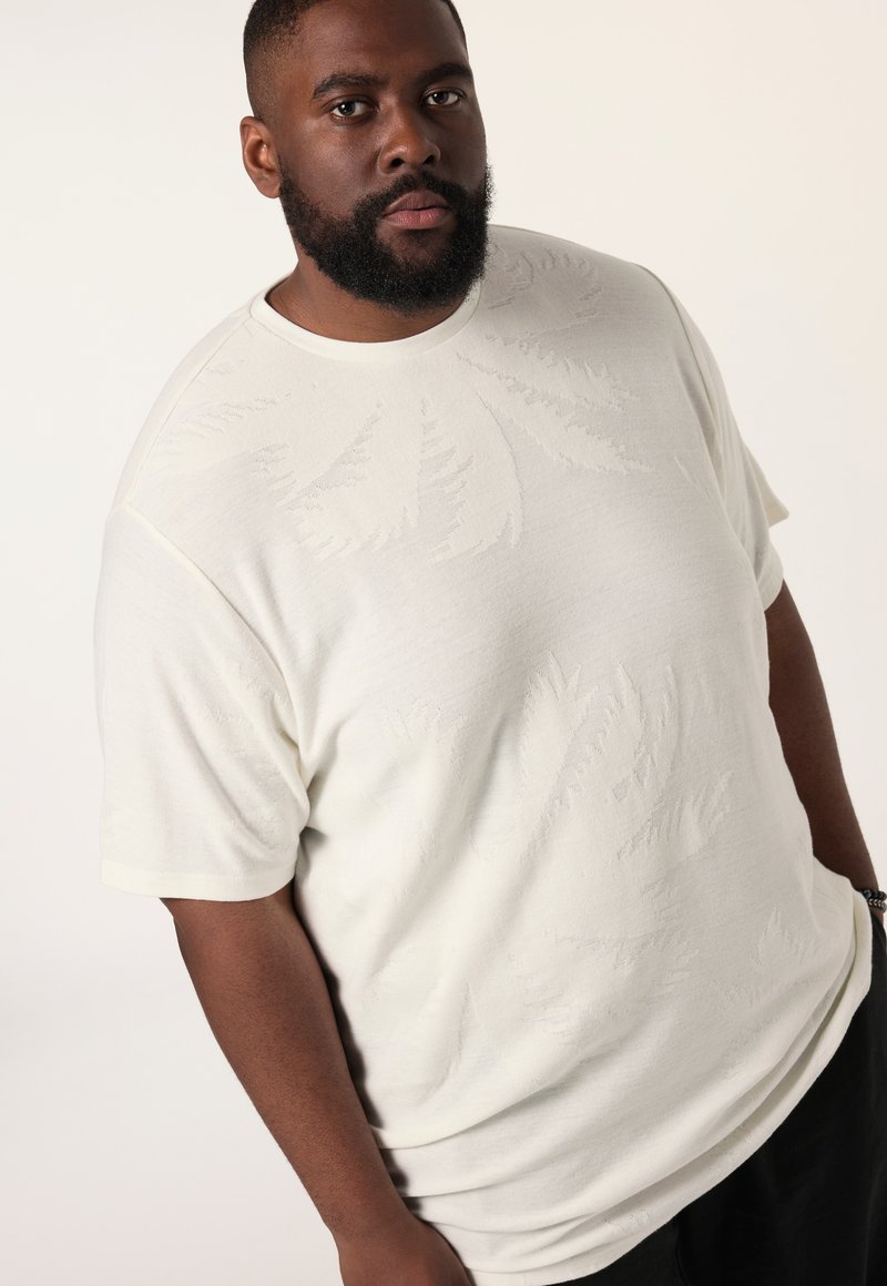 Camiseta de manga corta color crema con un patrón de hojas texturizado, cuello redondo y corte relajado, fabricada con un tejido suave y transpirable.