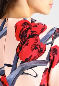 Blomstermønstret kjole med store røde og sorte blomster på en lys pink baggrund, med en slank lynlåsdetalje bagpå.