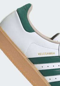 Weiße Leder-Sneaker mit grünen Akzenten, ausgestattet mit einer strukturierten Gummisohle, horizontalen Streifen und dem eingeprägten Schriftzug "VELOSAMBA" in Gold.