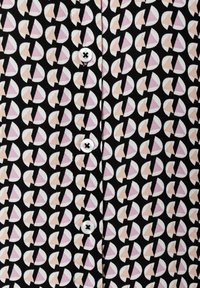 Chemise multicolore présentant un motif géométrique de cercles rose clair, blanc et noir ; comprend des boutons blancs avec un centre noir.