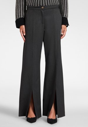 Dunkelgraue, weit geschnittene Hose mit vorderen Schlitzen, kombiniert mit schwarzen spitzen Schuhen und einem strukturierten Stricktop mit umgeschlagenen Bündchen.