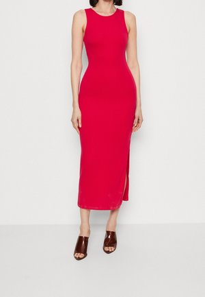 Mouwloze aansluitende rode midi-jurk met zijsplit, gedragen met bruine open-teen hakken door een staande persoon tegen een effen achtergrond.