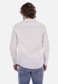 Camicia bianca in lino a maniche lunghe con polsi abbottonati, colletto classico e orlo curvo; cuciture dettagliate lungo il retro e le spalle.