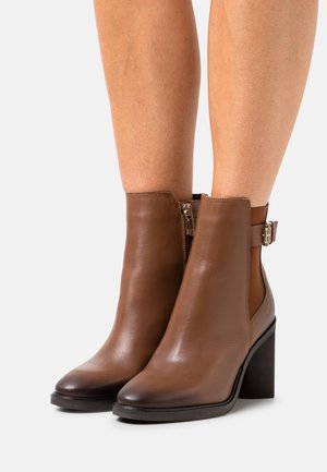 Bottines en cuir marron avec talon bloc, fermeture éclair sur le côté et détail boucle. Texture lisse et design à bout effilé.