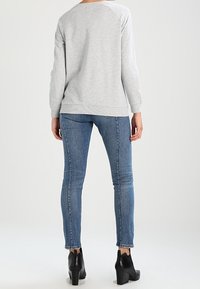 Felpa grigia oversize con maniche raglan, abbinata a jeans aderenti blu e stivali neri alla caviglia. Design semplice e dettagli minimi.