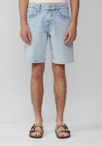 Shorts en jean bleu clair à coupe droite, dotés de cinq poches, d'une fermeture à bouton et de ourlets retroussés. Portés avec des sandales marron.