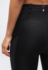 Κοντινό πλάνο ενός ατόμου που φοράει μαύρα κολάν με ψηλή μέση, με εμφανή ραφή και μια μικρή ετικέτα με το λογότυπο στη μέση.