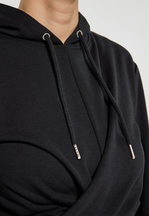 Schwarzer Kapuzenpullover mit weicher Textur, mit Kordeln und silbernen Tipps, der ein gedrehtes Vorderdesign aufweist, das einen geschichteten Effekt erzeugt.