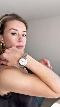 Ασημένιο ρολόι από ανοξείδωτο ατσάλι με στρογγυλή λευκή διάταξη και τρία υποδείκτες, φορεμένο σε καρπό με ανοιχτόχρωμο δέρμα, σε ουδέτερο φόντο.