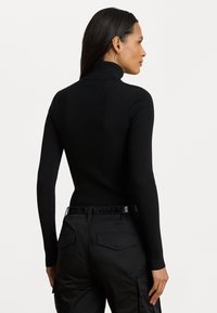 Melnas ribotās augstās apkakles džemperis ar garām piedurknēm, pieguļošs dizains. Valkāts ar melnām augstā jostasvietā uzvalka biksēm ar kabatām.