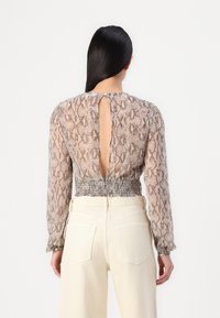 Blusa a maniche lunghe con stampa a serpente, caratterizzata da vita smock e dettaglio a chiave sul retro, realizzata in tessuto leggero.