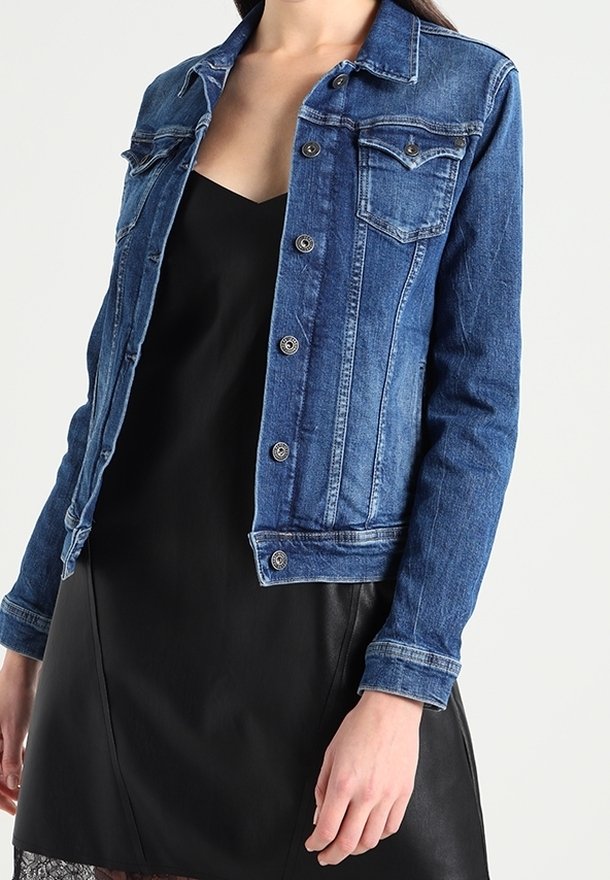 Jeansjack in medium blauw met lange mouwen, voorzakken, knoopsluiting en een vervaagde textuur. Gelaagd over een zwarte jurk.