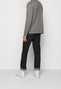 Grå långärmad tröja med avslappnad passform, i kombination med mörkblå denimjeans med uppvikta muddar, kompletterad med vita sneakers.