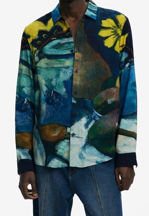Chemise à manches longues avec boutons, à imprimé abstrait et coloré de formes bleues, jaunes, vertes et marron, portée avec un jean bleu.
