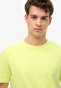 Camiseta de algodón amarillo neón con cuello redondo y mangas cortas, que presenta una textura suave y un diseño sencillo.