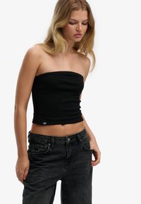 Top corto negro sin tirantes hecho de una mezcla elástica de algodón, con un diseño ajustado y una textura suave. Combinado con jeans negros de tiro alto.