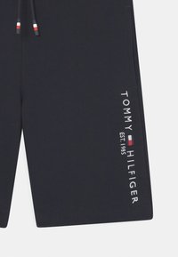 Granatowe szorty z troczkami, z czerwonymi, białymi i niebieskimi końcówkami oraz białym tekstem z logo Tommy Hilfiger oraz flagą na dolnej części nogawki.