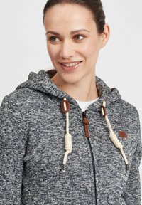 Kapütsiga sviiter tekstureeritud hallist ja tumesinisest kangast. Omab valgeid nöördrawstringe pruuni aktsendiga ning ees on lukk.