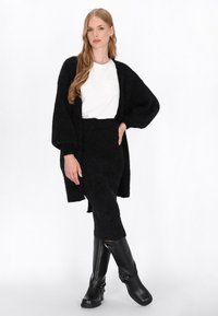 Czarny dzianinowy kardigan z oversize'owymi rękawami, w zestawieniu z białym t-shirtem i dopasowaną czarną dzianinową spódnicą. Czarne kozak do kolan.