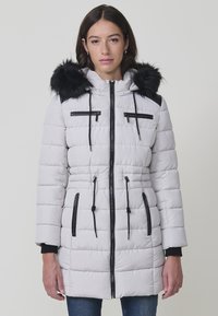 Abrigo acolchado gris claro con capucha con borde de piel, cremalleras negras, cordones ajustables y dos bolsillos frontales. Diseño ajustado.
