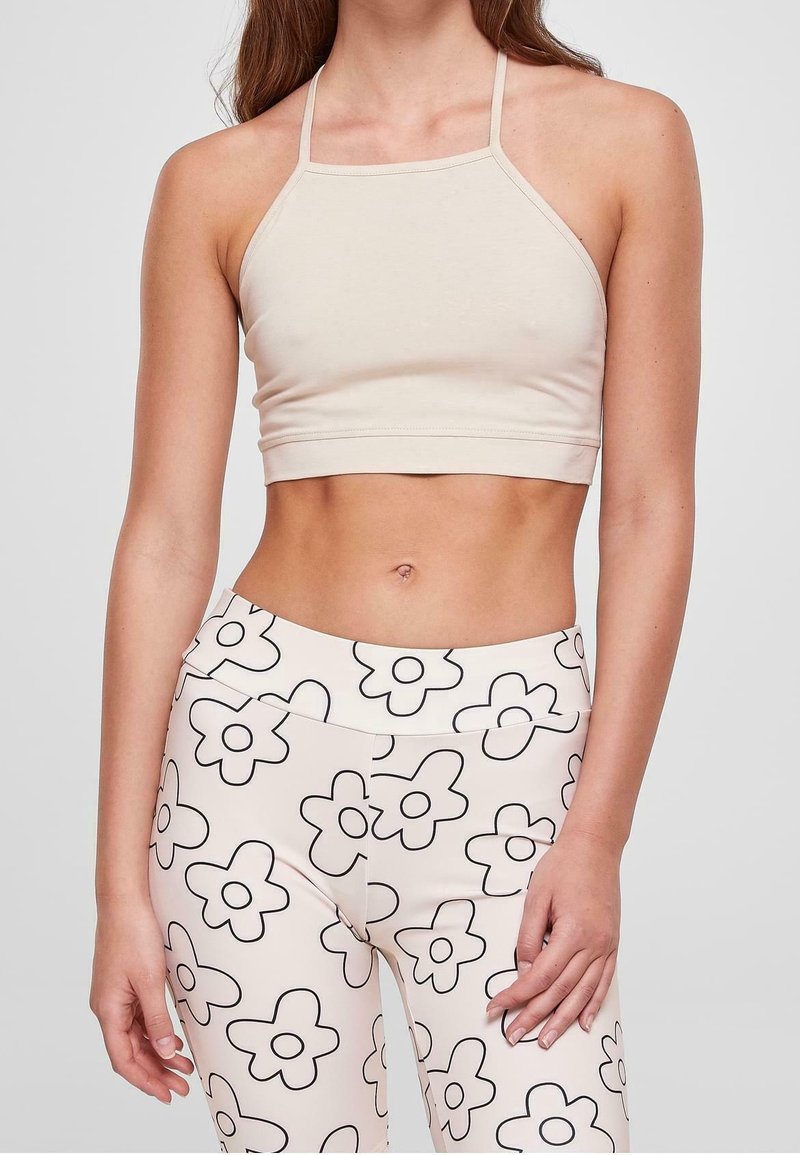 Top corto beige con spalline sottili, abbinato a leggings a vita alta con un motivo floreale nero su uno sfondo chiaro.
