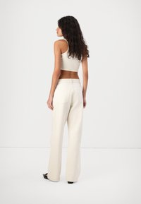 Wide-leg, off-white pants made from denim with back pockets and a fitted cropped top. Curly hair and a neutral backdrop complete the look.