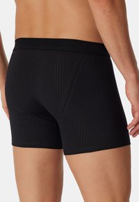 Černé ribbed boxerky mají přiléhavý střih s měkkým elastickým pasem. Texturované vzory se směrem dolů zpevňují celkový vzhled.