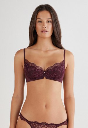 Reggiseno in pizzo di un borgogna scuro con bordi decorativi a scallop, spalline regolabili e un piccolo accento decorativo centrale. Perizoma in pizzo abbinato.