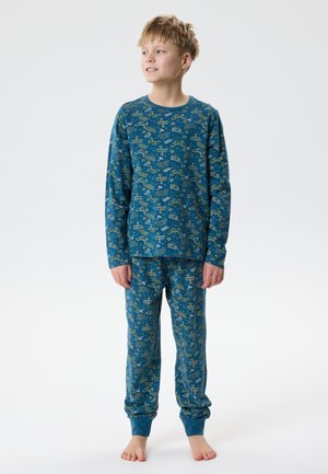 Fant deček, bos, oblečen v modre pižame z vzorcem igralnega krmilnika in robota, gleda levo.