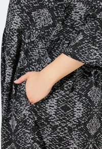 Schwarzes und graues gemustertes Kleid mit lässigem Schnitt, kurzen Ärmeln und einer seitlich in den fließenden Stoff integrierten Tasche.