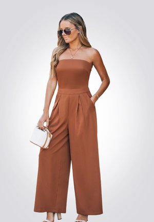 Combinaison marron sans bretelles avec des jambes larges, un design plissé et un corsage ajusté. Assortie à un sac à main blanc et des lunettes de soleil.