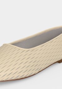 Μπεζ επίπεδο παπούτσι με διαγώνιο διάτρητο σχέδιο και στρογγυλεμένη μύτη, με εσωτερική επένδυση ανοιχτού γκρι χρώματος και λεπτή σόλα.