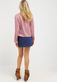 Blouse à manches longues rose à motifs, associée à une jupe en denim bleue. Bottines en daim marron avec des franges ; texture lisse, design ajusté.