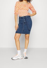Denim pencil skirt with tie waist detail, paired with an orange floral crop top. Model wears white sneakers and ruffled ankle socks.